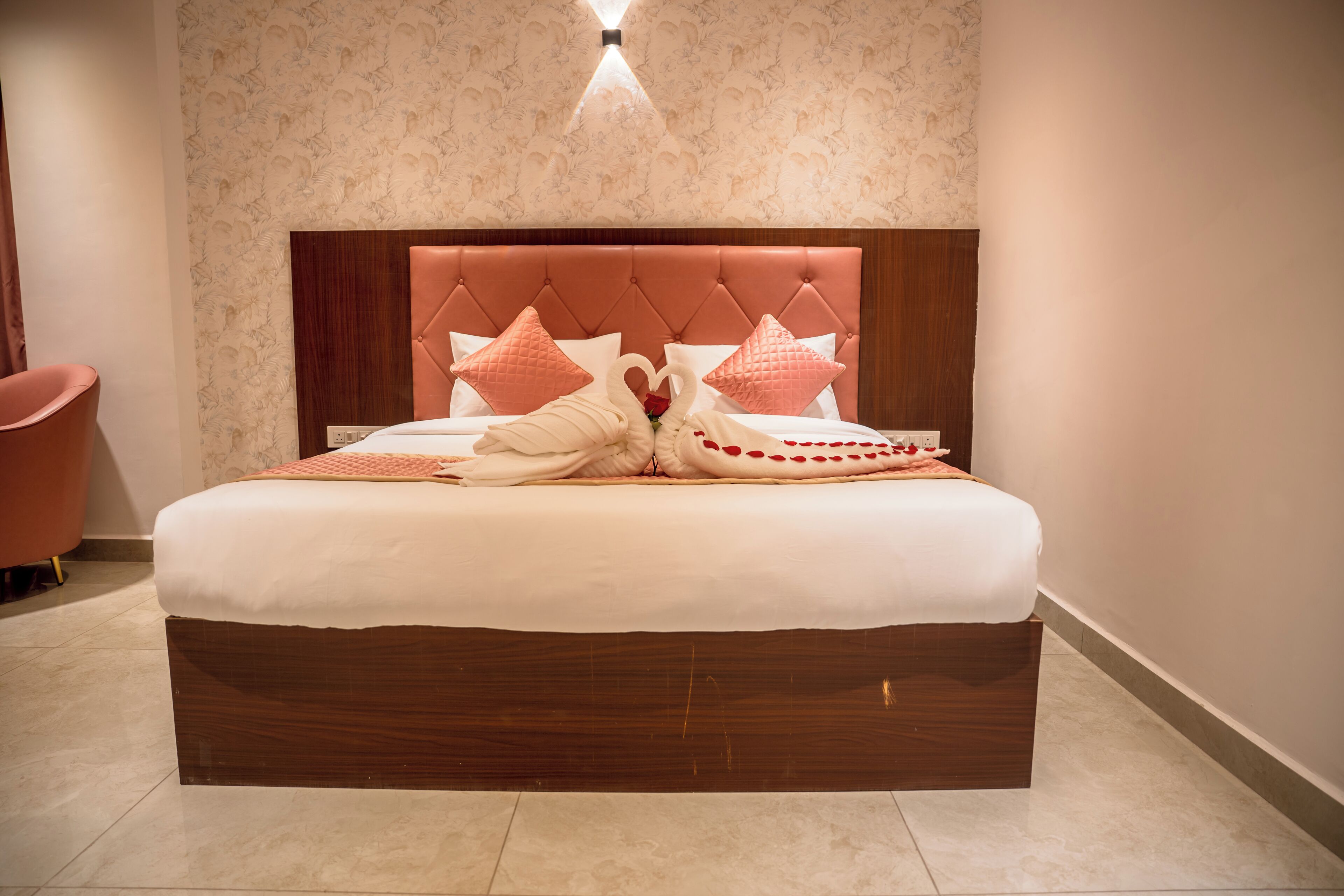 Un lit bien fait, avec une tête de lit en bois, deux oreillers roses et une composition décorative représentant des cygnes posée sur le couvre-lit.
