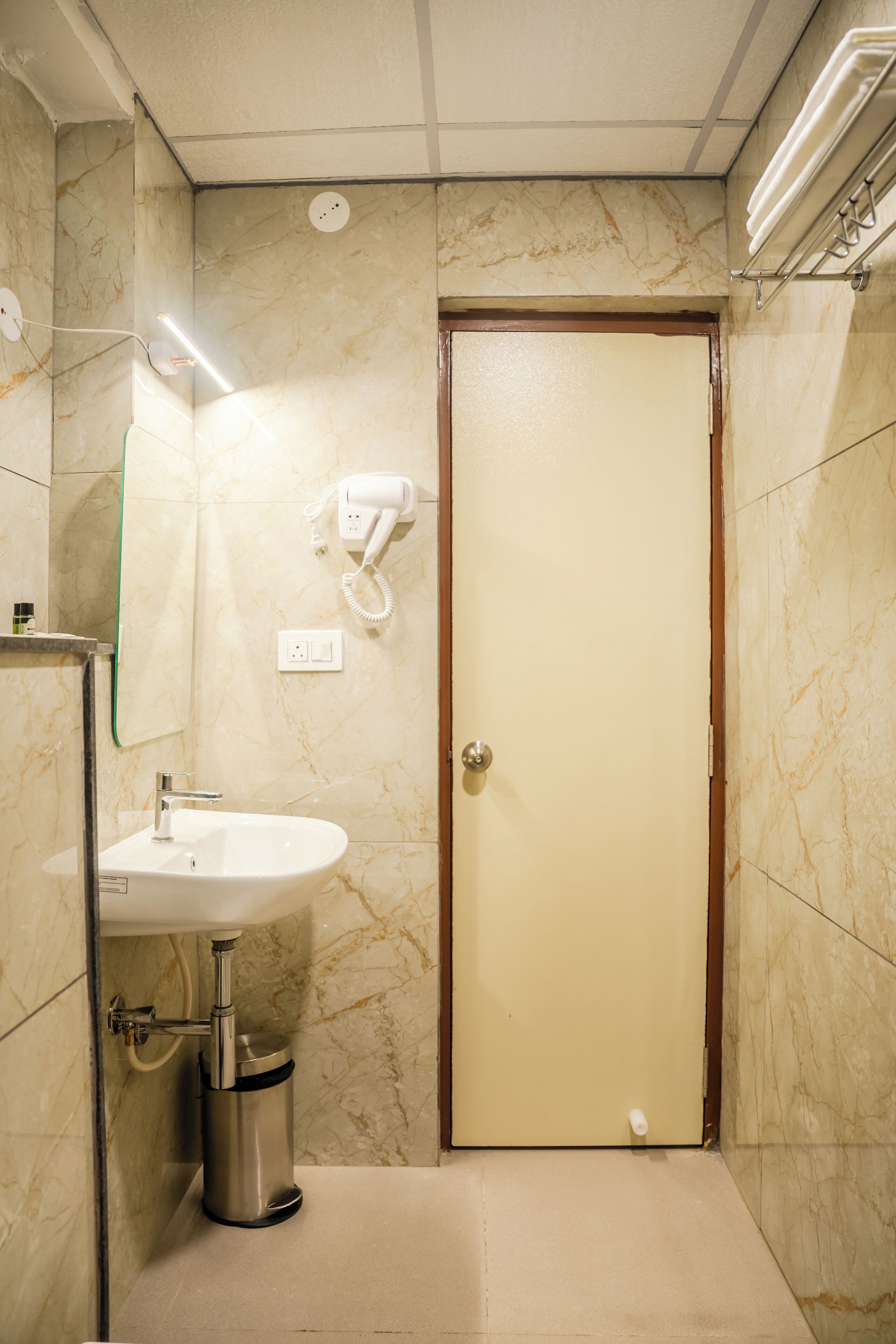Un baño con pared de mármol, un lavamanos, un secador de pelo y un cubo de basura.