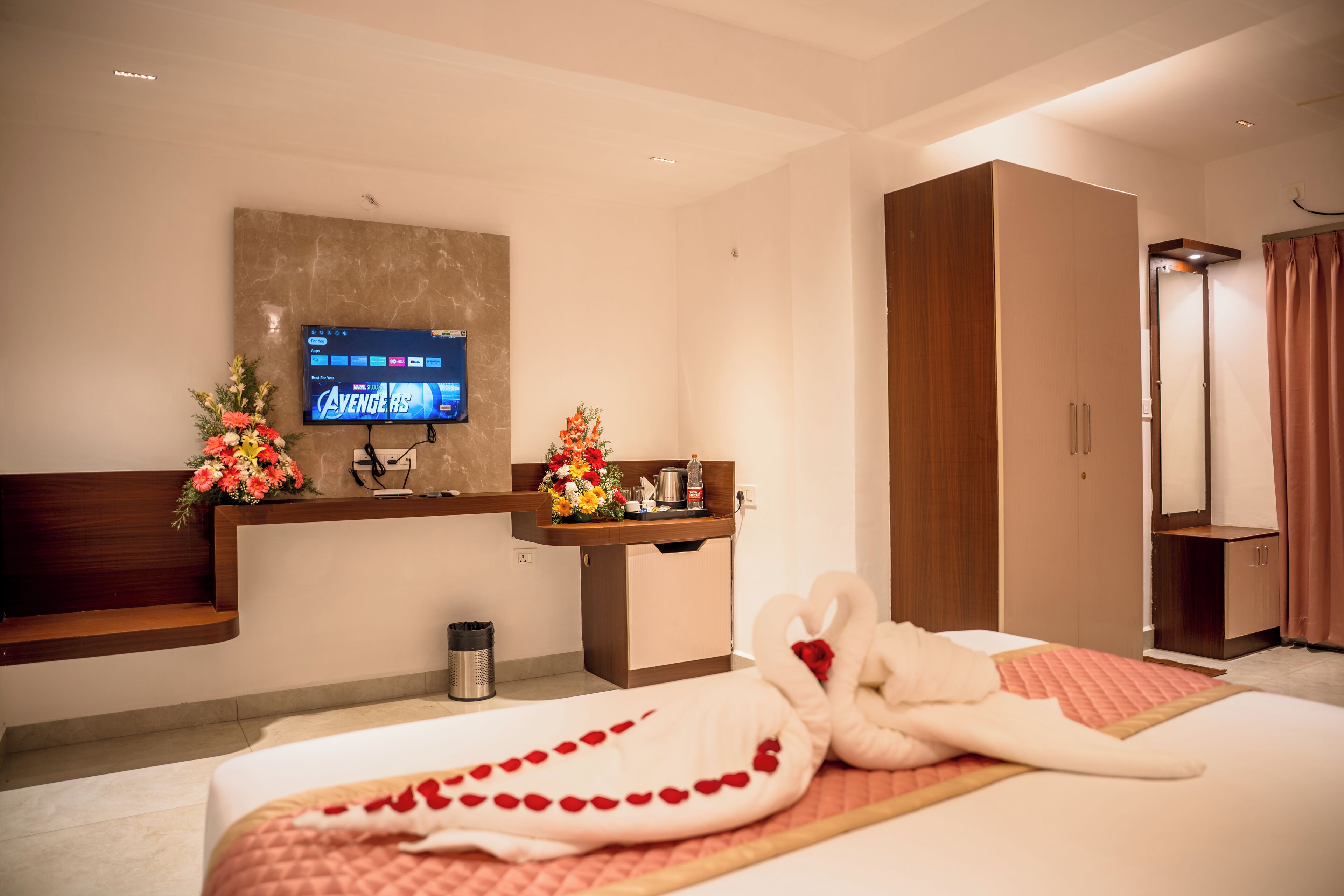A hotel room with a bed, a TV on the wall, a desk with a computer, and a wardrobe.