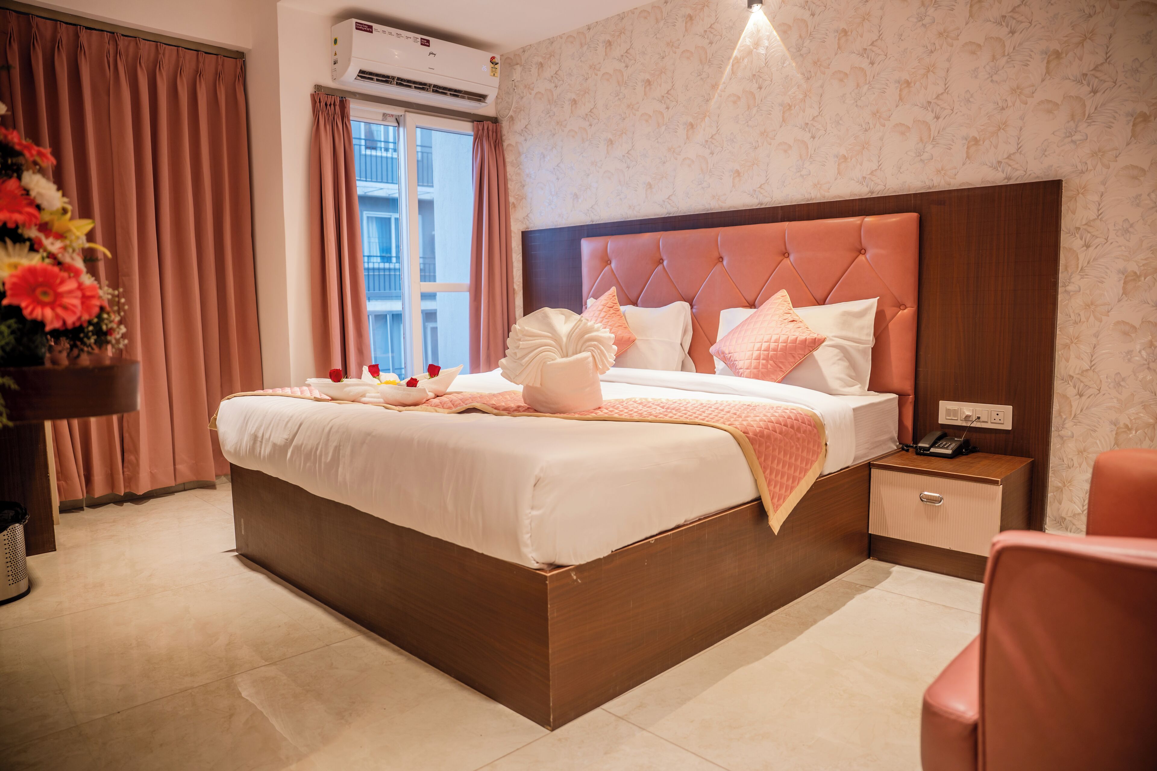 A neatly made bed with a headboard, a bedside table with a lamp, and a window with curtains.