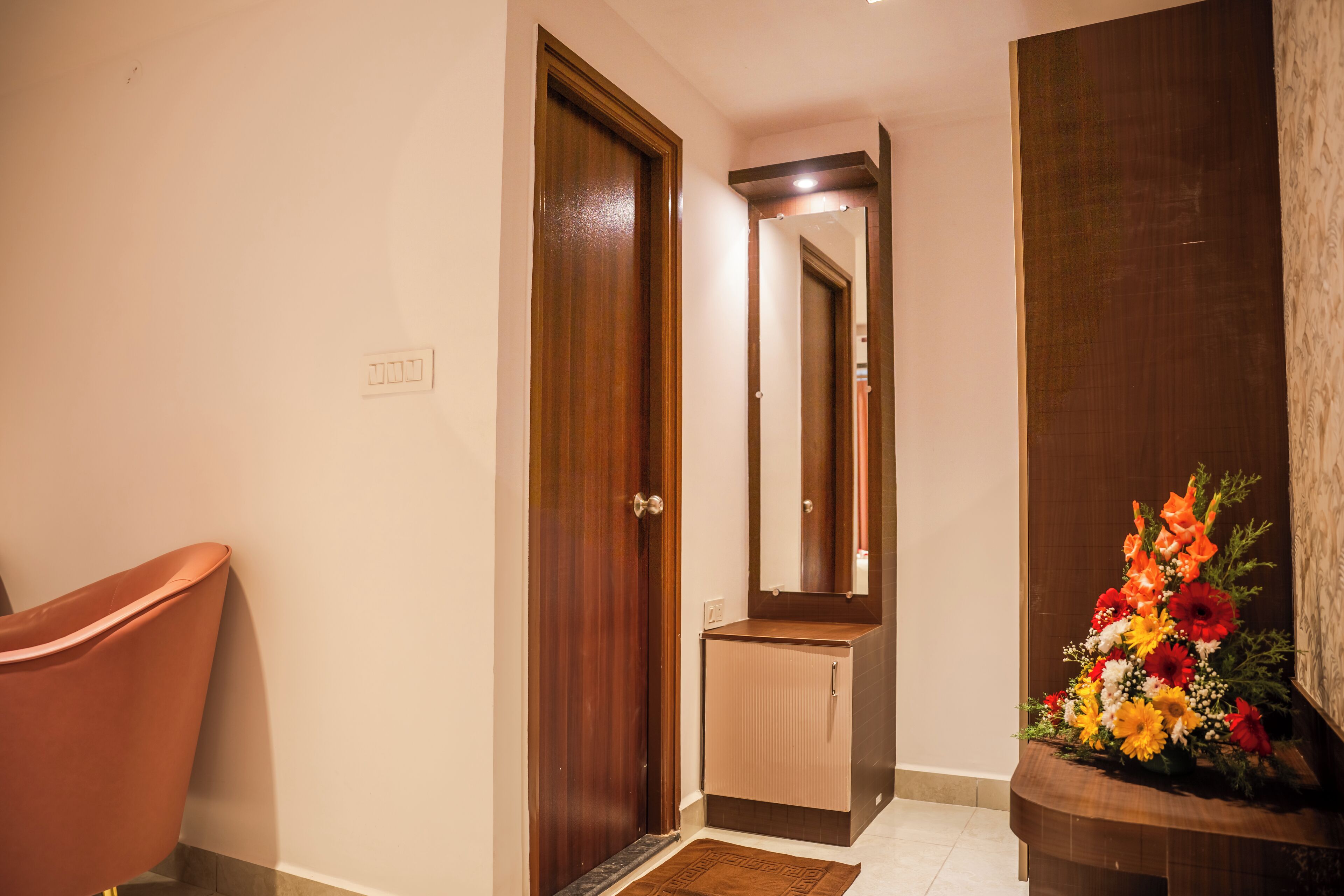 A hallway with a wooden door, a small cabinet, a mirror, and a floral arrangement.