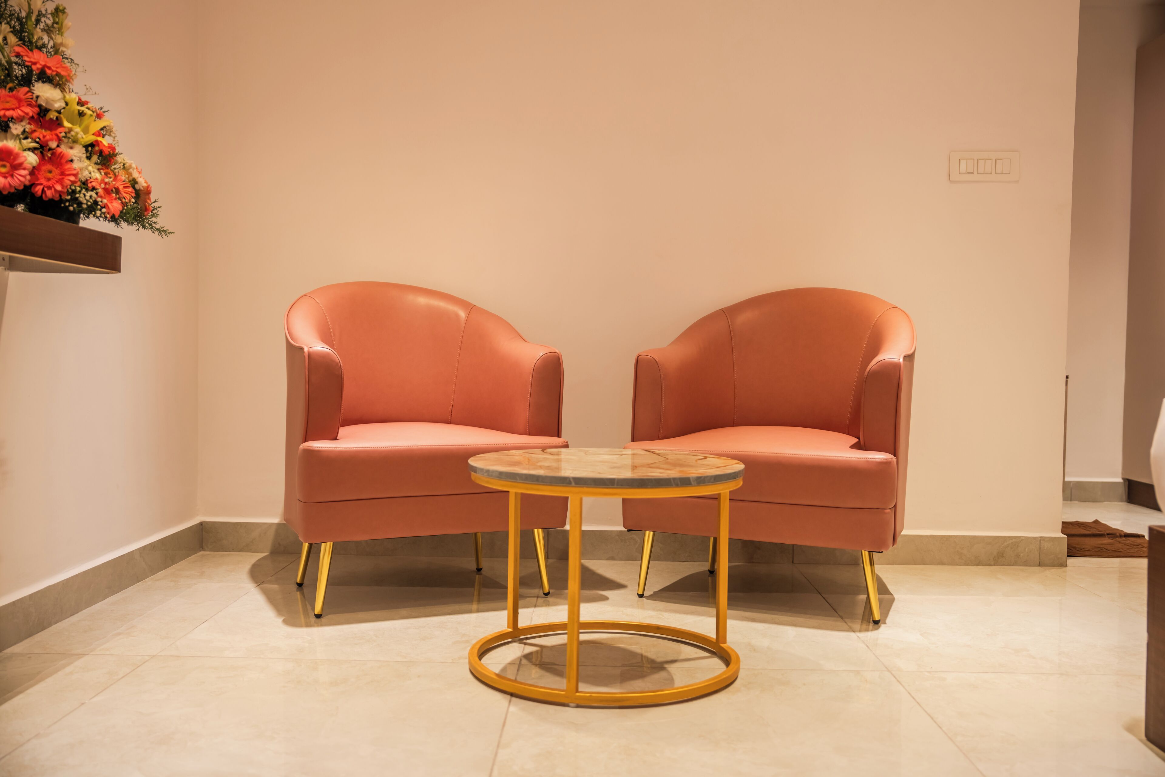 Quarto com duas cadeiras laranja e uma mesa redonda com tampo de vidro e pés dourados.