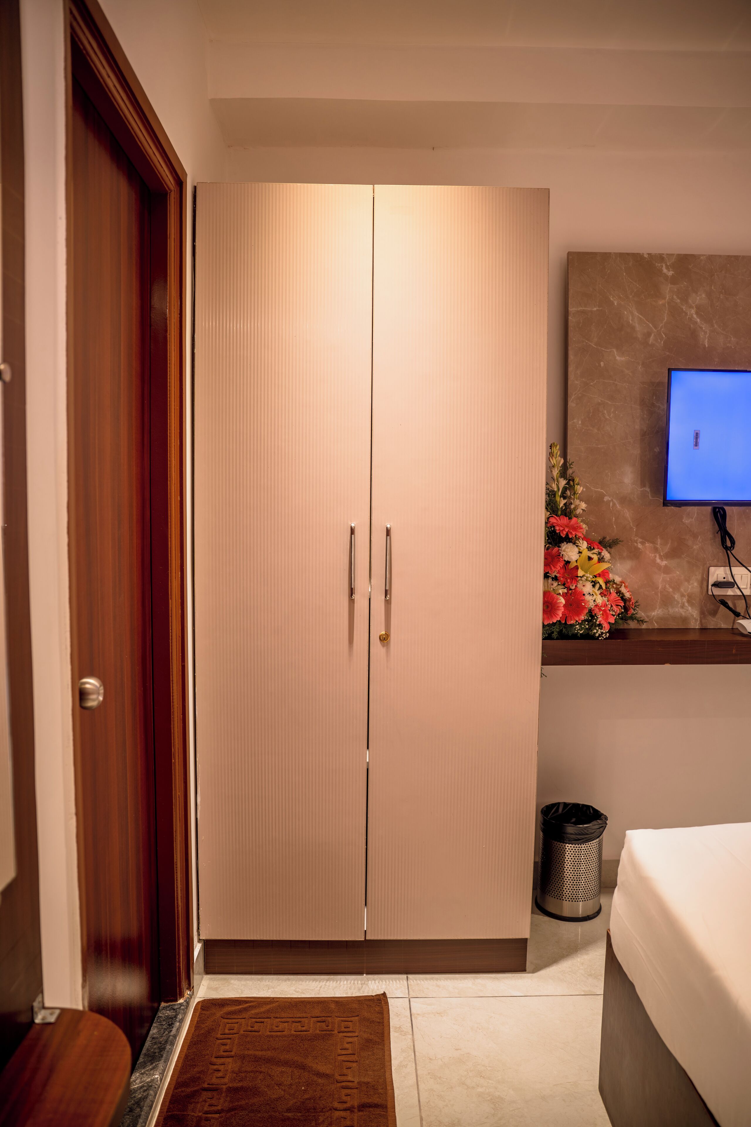 A bedroom with a bed, a wardrobe, a television, and a small trash bin.