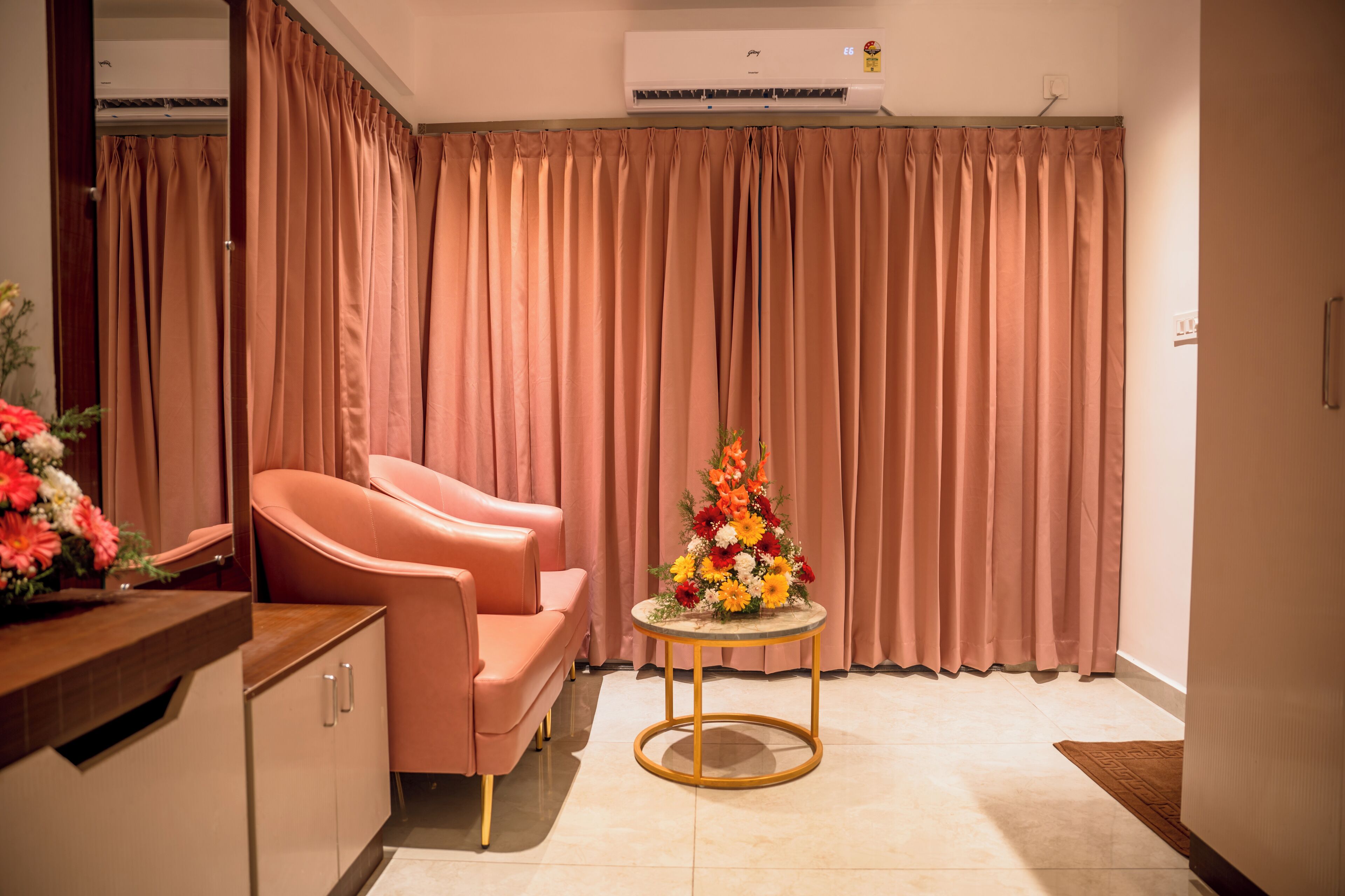 Een kamer met een roze bank, een ronde tafel met bloemen en een gordijn als achtergrond.