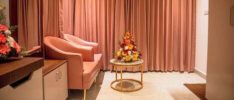 A room with a pink sofa, a round table with a flower arrangement, and a curtain backdrop.