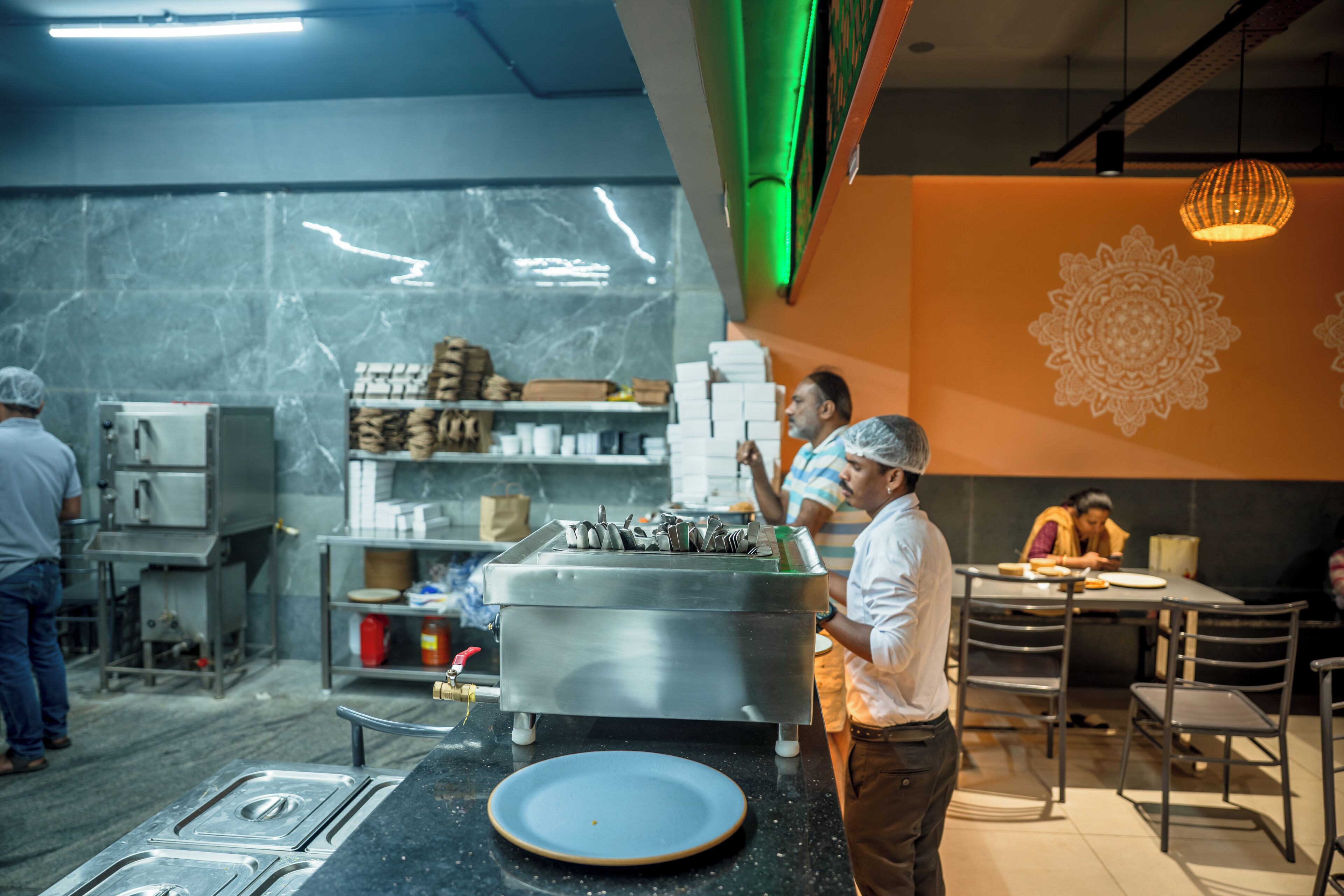 Une cuisine professionnelle équipée d’appareils en acier inoxydable, une assiette bleue posée sur le comptoir et un motif décoratif sur le mur.