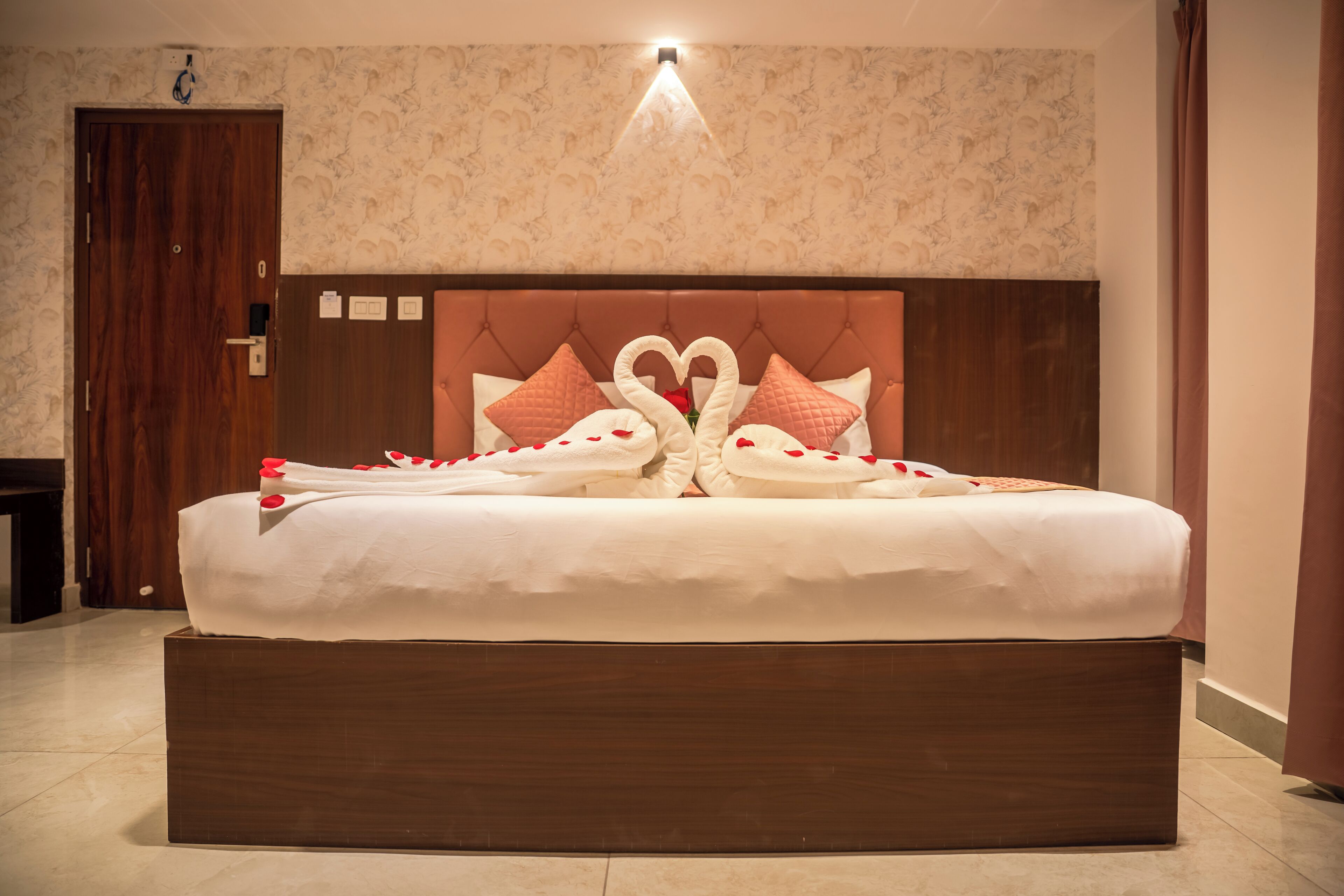 A large bed with a wooden headboard, a wall-mounted light fixture above, and a door to the left.