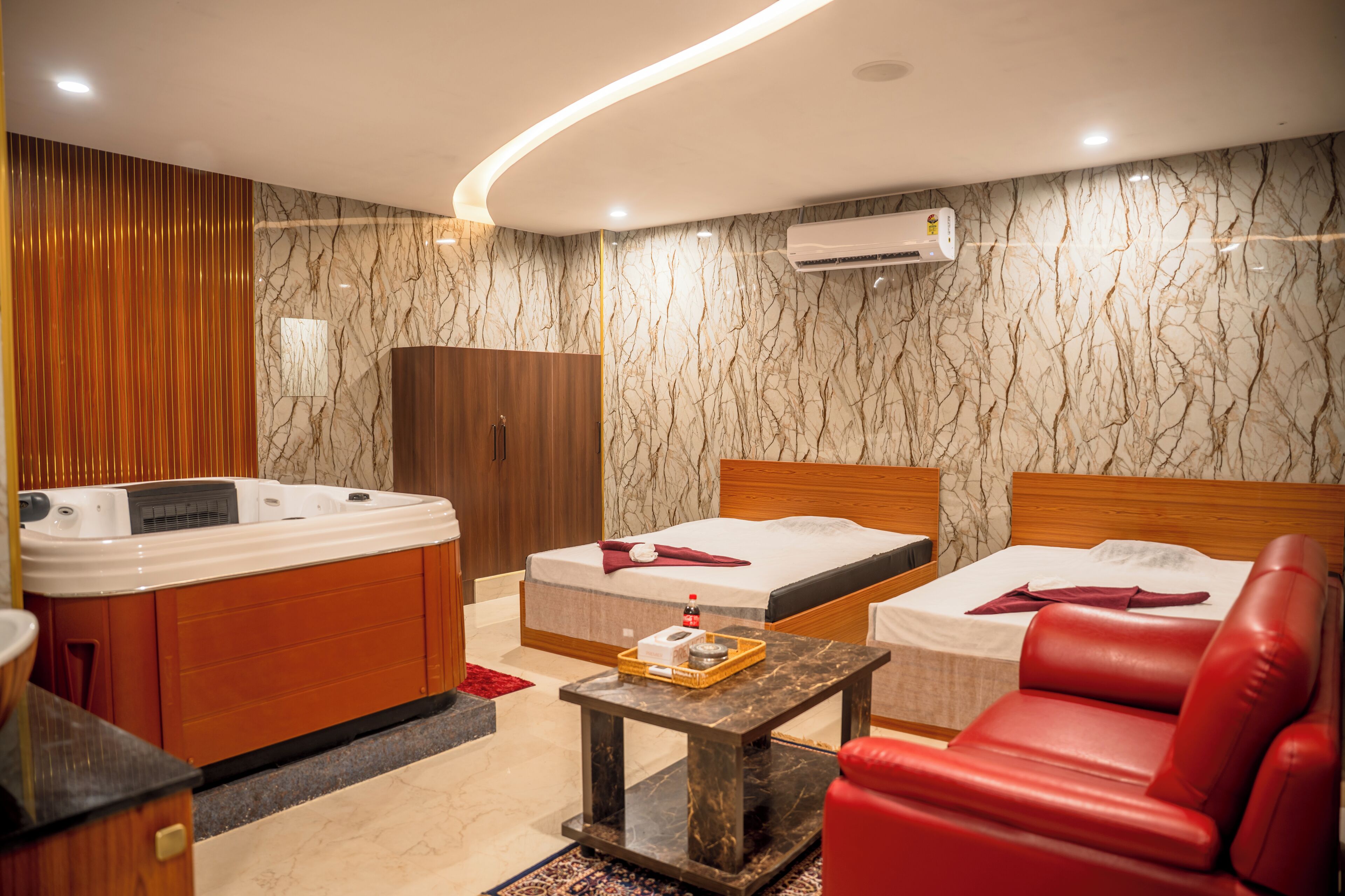 A hotel room with a wooden wardrobe, a bed with a red blanket, a red leather sofa, a small table with a tray, and a marble-patterned wall.