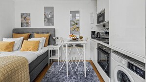 A modern bedroom with a bed, bedside table, and a small kitchenette with a washing machine. - Entire Malmö guest house with private terrace, king bed & free parking (Malmö)