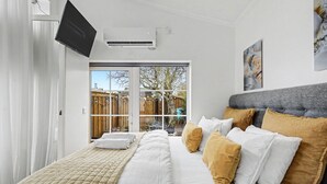 A bedroom with a bed, a flat-screen TV, an air conditioner, and a view of the outside. - Entire Malmö guest house with private terrace, king bed & free parking (Malmö)