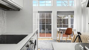 A modern kitchen with a large window, a dining area with a table and chairs, and a cozy seating area with a chair and a tripod. - Entire Malmö guest house with private terrace, king bed & free parking (Malmö)