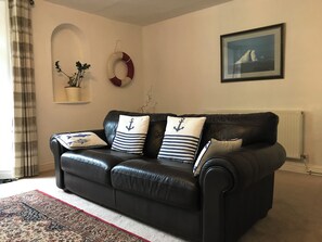 A black leather sofa with nautical-themed pillows, a patterned rug, a potted plant, and a framed picture on the wall. - Spacious self contained historical apartment in a central and level location (Falmouth)