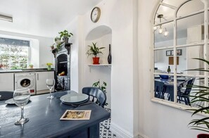 A dining area with a table set for two, a black and white patterned floor, a white wall with a clock, and a window with a view of the outside. - Spacious self contained historical apartment in a central and level location (Falmouth)