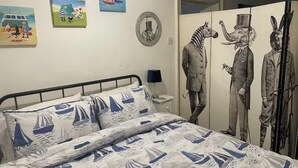Une chambre à coucher avec un lit orné d’un motif de voilier, une table de chevet avec une lampe, et des œuvres d’art murales comprenant une peinture représentant un voilier et une statue de zèbre.