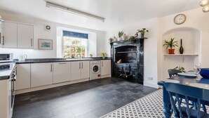 Une cuisine moderne avec des meubles blancs, une cuisinière noire et un coin repas doté de chaises bleues.