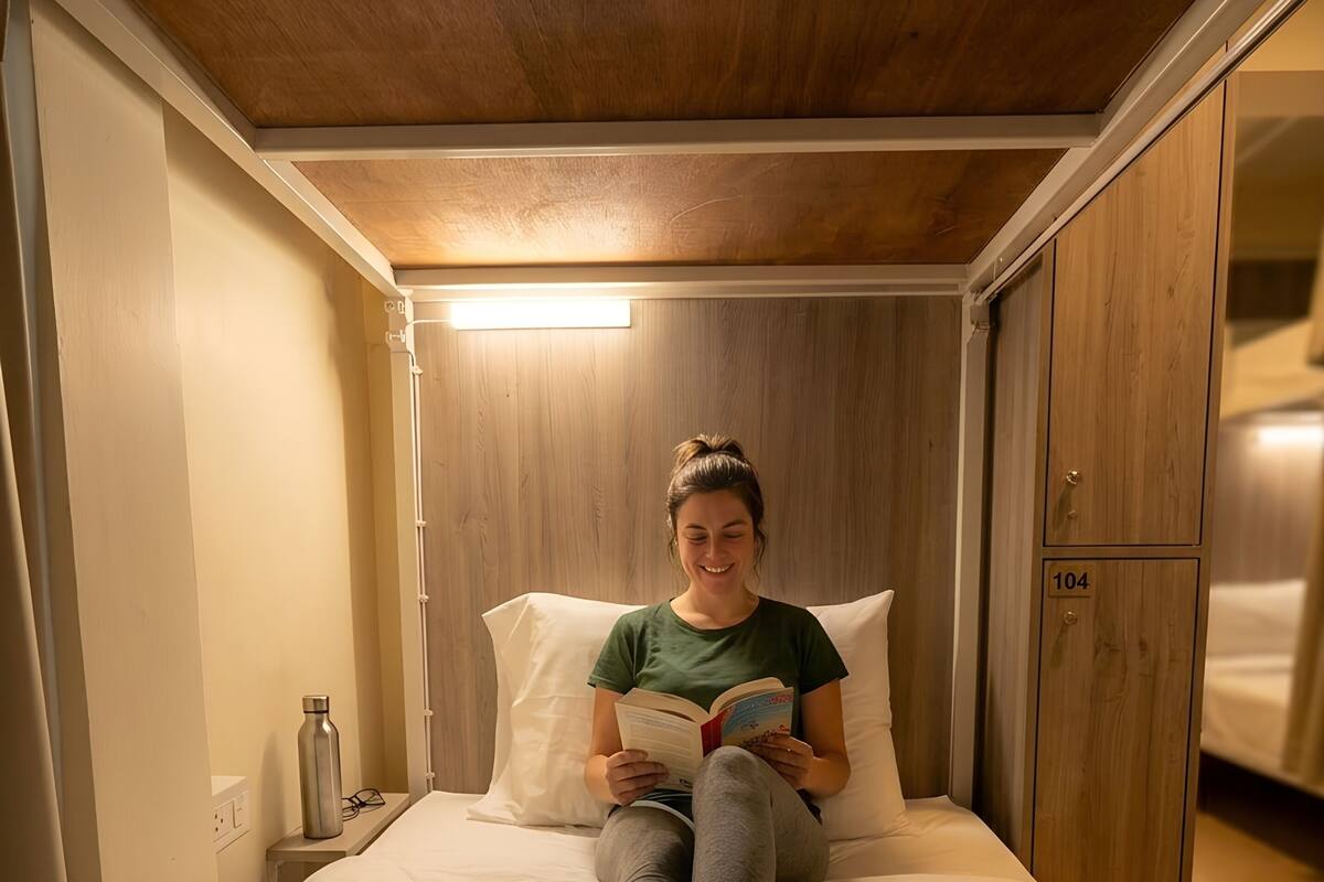 Una persona sentada en una cama en una habitación con paredes y techo de madera, leyendo un libro.