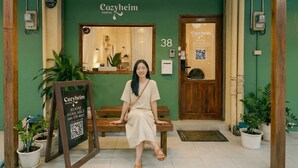A person sitting on a bench outside a hostel named 'Cozyheim'.