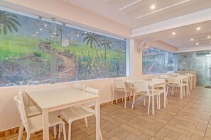 A restaurant with white tables and chairs, a large mural of a tropical landscape, and a modern ceiling design. - Hotel O by OYO New Hotel Hamsa (Hyderabad)
