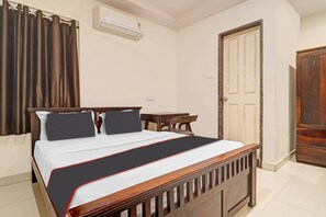 A hotel room with a wooden bed, a small table, a door, and an air conditioning unit on the wall. - Hotel O by OYO New Hotel Hamsa (Hyderabad)
