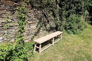 A wooden bench in a grassy area with a stone wall and dense foliage in the background. - Complete accommodation: Apartment in Gemünden, Germany (Gemünden)