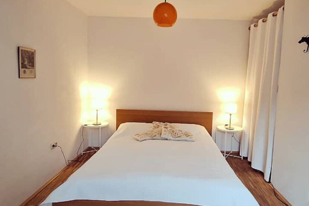 A neatly made bed with a white duvet, two bedside lamps, and a single hanging light fixture.