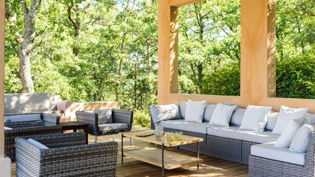 Een terras met rieten meubels, een tafel met glazen blad en een comfortabele zithoek.
