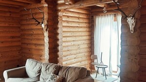 Interior de una cabaña de troncos con un sofá, una mesita redonda y cuernos de ciervo montados en las paredes.