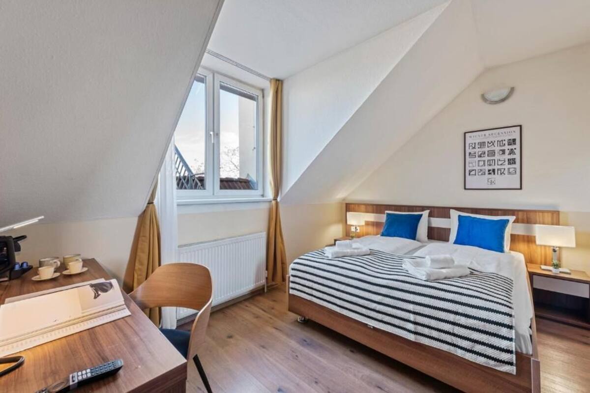 A bedroom with a bed, bedside tables, a desk, and a window.