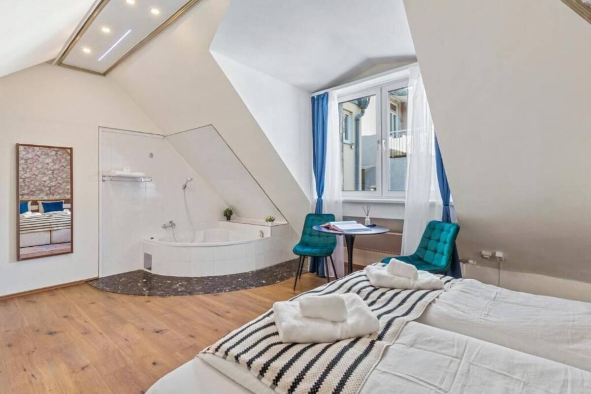 A bedroom with a large bed, a sitting area with a table and chairs, a bathtub, and a window with curtains.