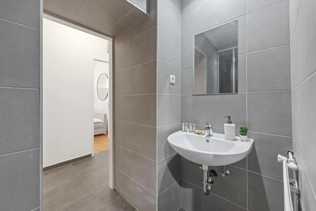 A modern bathroom with grey tiles, a white sink, and a mirror.
