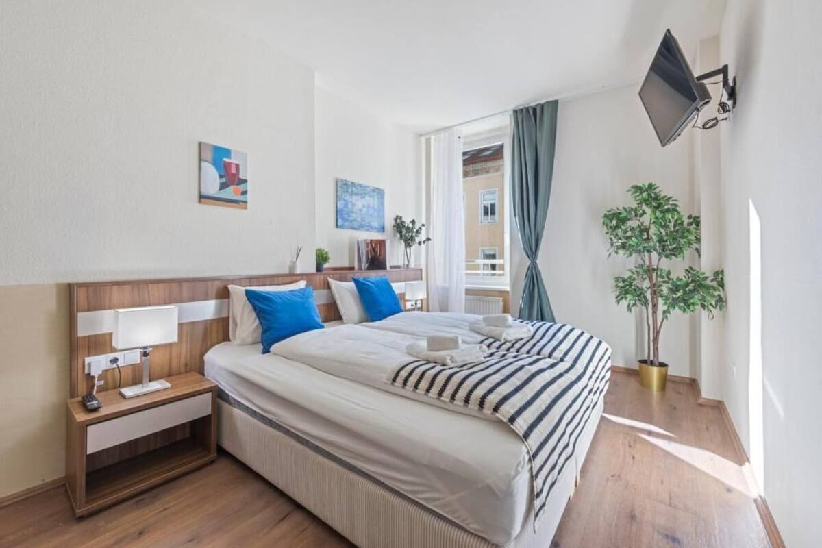 A hotel room with a large bed, bedside tables, a TV mounted on the wall, and a potted plant.