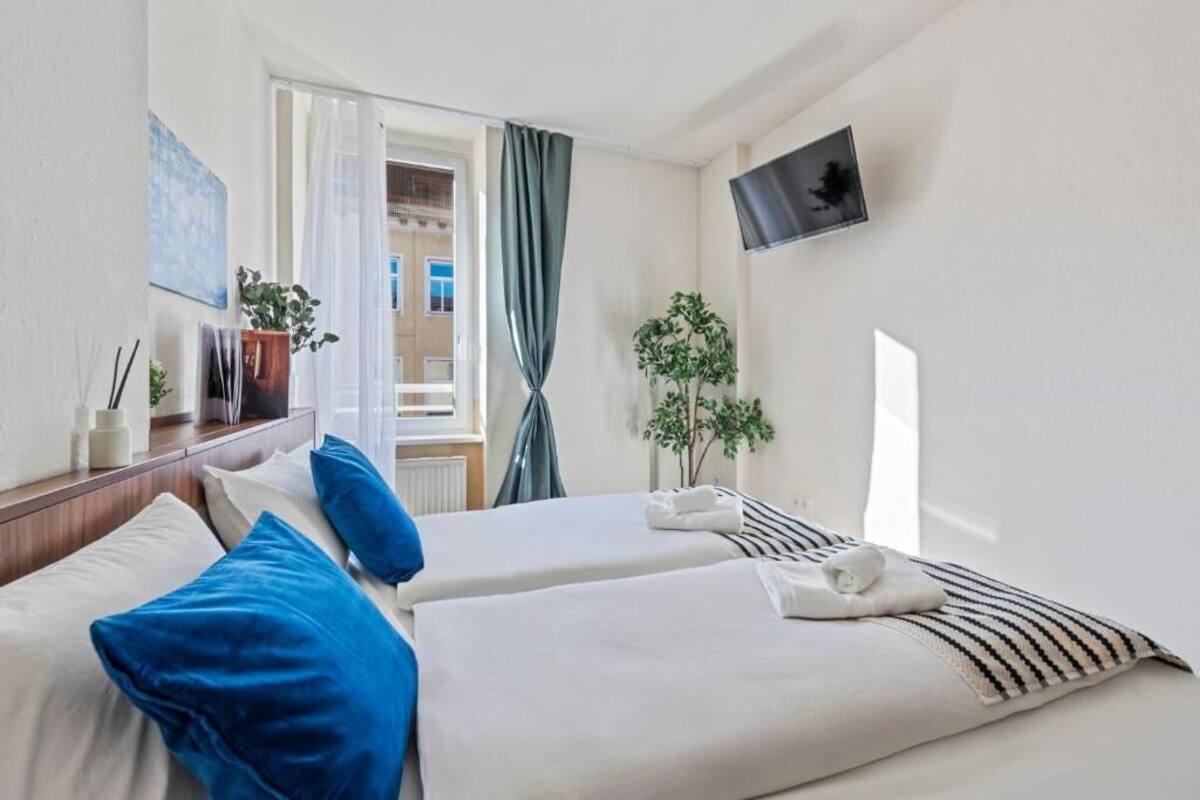 A hotel room with two beds, a TV, a window with curtains, and a plant.