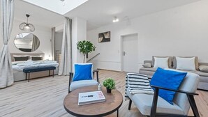 Una sala de estar moderna y bien iluminada con sofá, sillones, una mesa de centro y una cama con un espejo grande.
