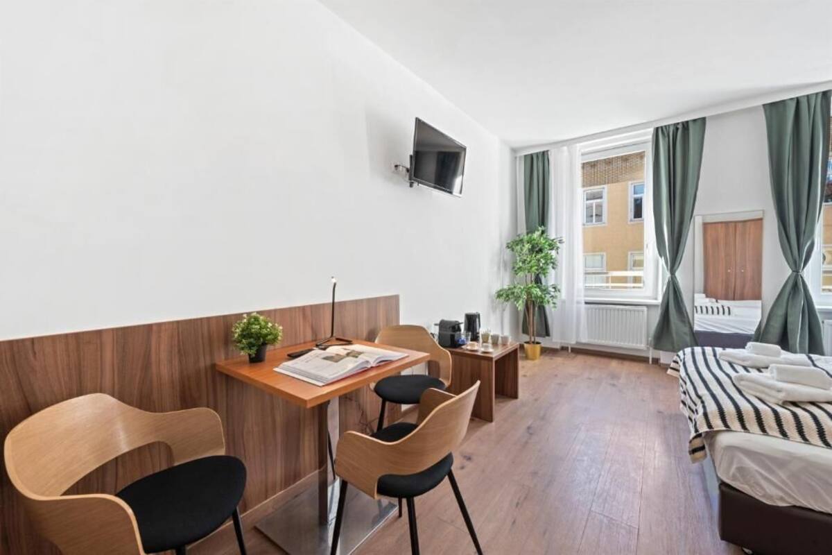 A hotel room with a wooden desk, two chairs, a bed, a TV, and a window with curtains.