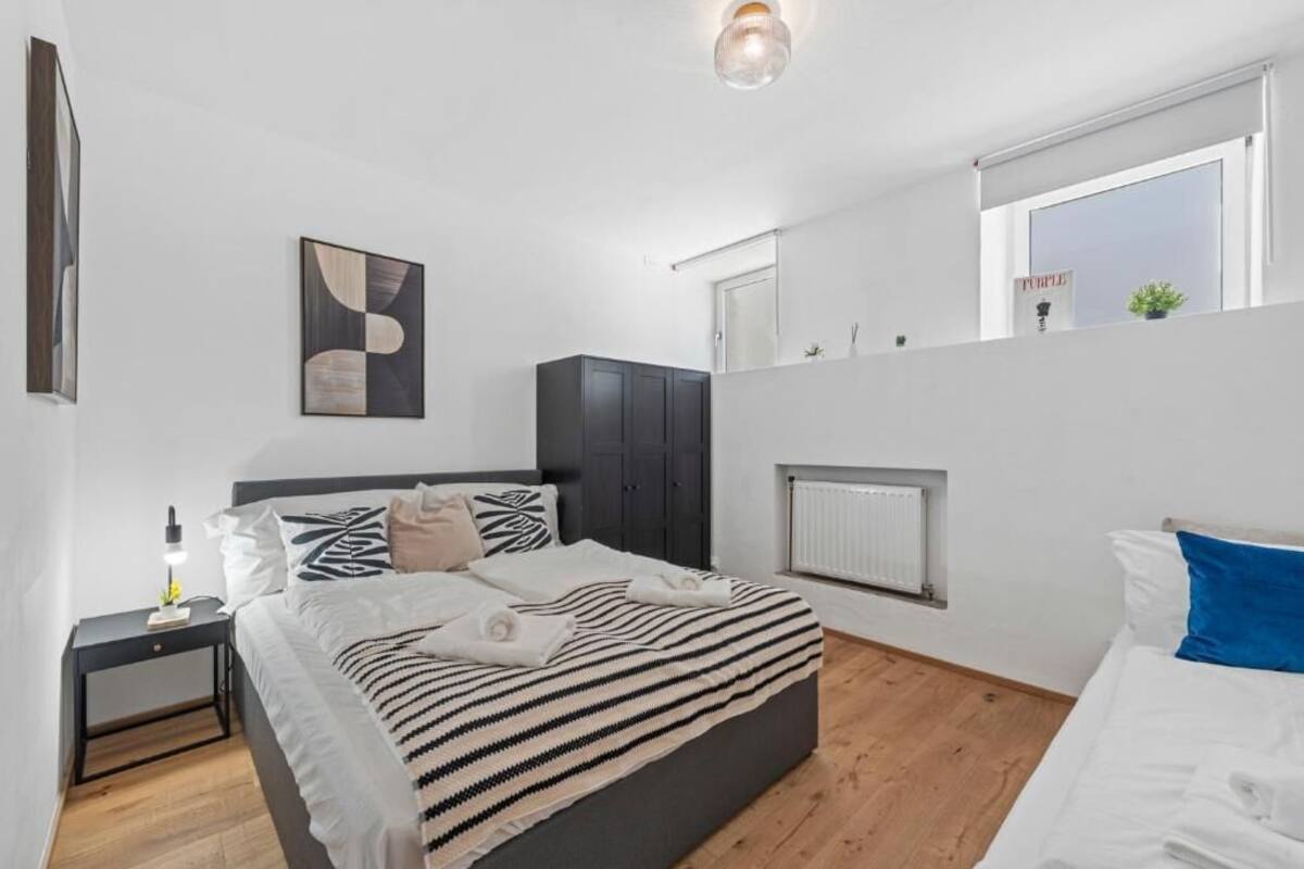 A modern bedroom with a large bed, a nightstand, a radiator, and a window.