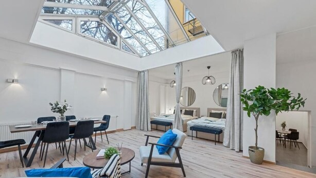 Amplia habitación con techo alto y tragaluz, que incluye un comedor, asientos y una cama.