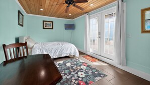 Een slaapkamer met een houten plafond, een bed met wit beddengoed, een aan de muur bevestigde televisie en een groot raam met gordijnen.