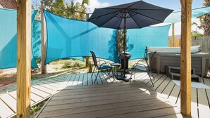 Een houten terras met een tafel, stoelen, een barbecue en een blauw zonnescherm.