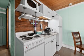 A compact kitchen with white appliances, wooden wall paneling, and a wooden ceiling. - Blue Angels Beach Bungalow (Pensacola)