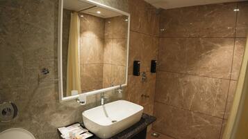 A modern bathroom with a marble-tiled shower, a white sink, and a large mirror.