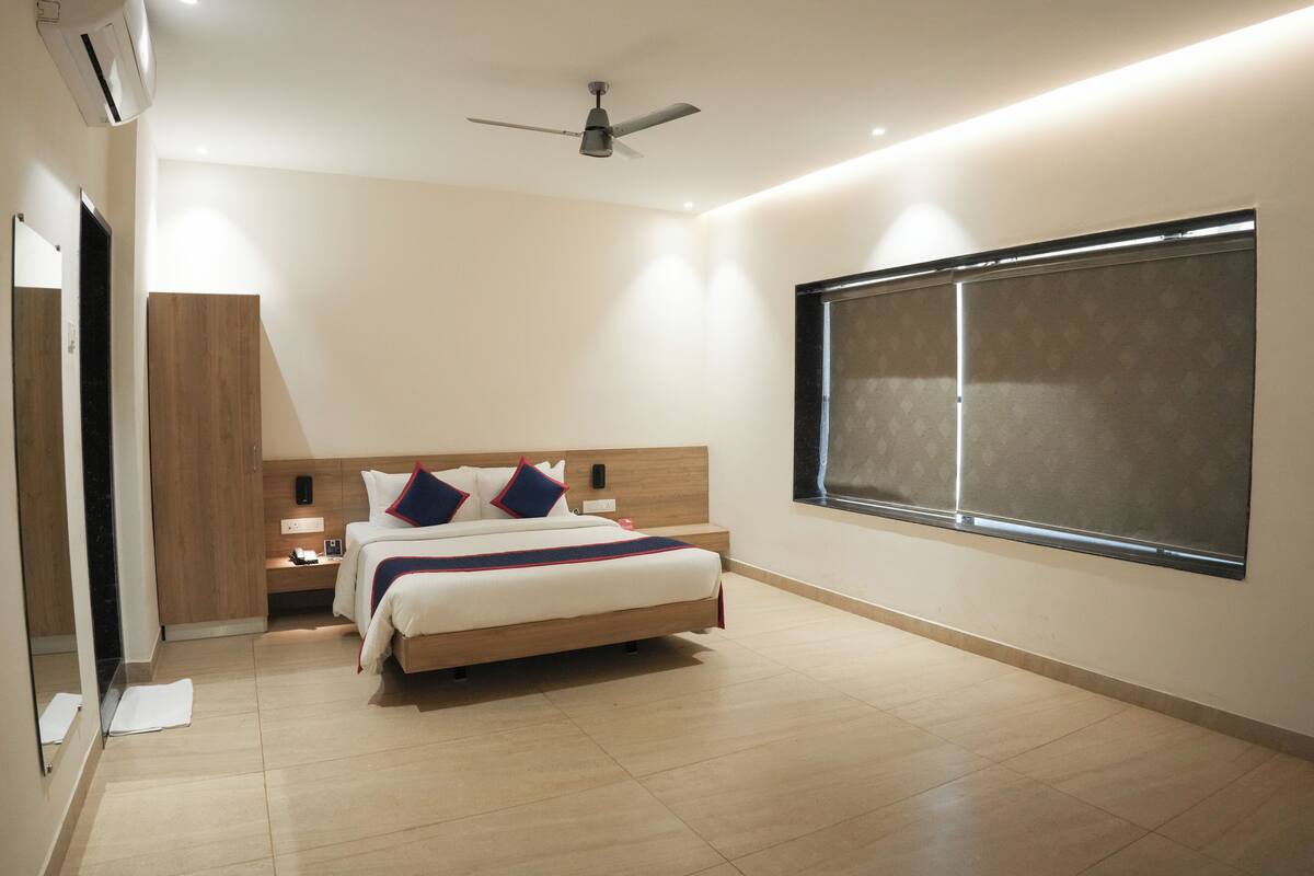 A modern hotel room with a bed, bedside table, nightstand, and a large window.