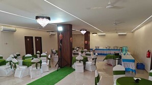 A conference room with round tables, chairs, and a stage area. - Hotel Shivam by Greenwoods Resorts (Kudal)