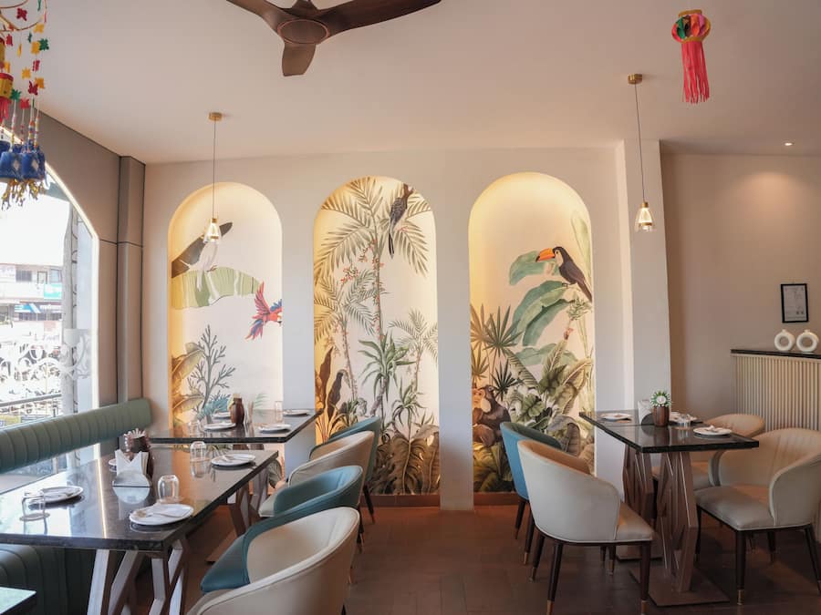 Ein Restaurant mit tropischem Wandgemälde, grünen Sitzgelegenheiten und Blick auf die Straße.