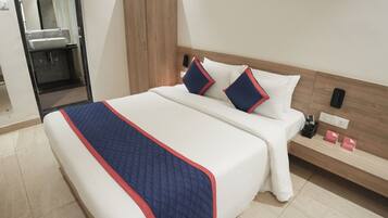 Habitación de hotel con cama, mesita de noche con teléfono y cargador, espejo y armario de madera.