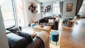 A modern living room with a leather sofa, a coffee table, and a dining area with a table and chairs. - Corsican Apartment Near Sandy Beaches (Ax-les-Thermes)
