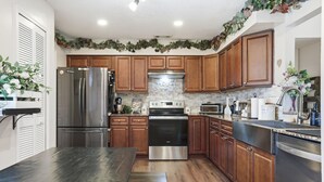 A kitchen with wooden cabinets, stainless steel appliances, and a stone backsplash. - Cozy Orlando getaway | Near Disney | Fenced Yard (Ocoee)