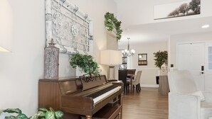 A piano, a dining table with chairs, a chandelier, and a white door. - Cozy Orlando getaway | Near Disney | Fenced Yard (Ocoee)