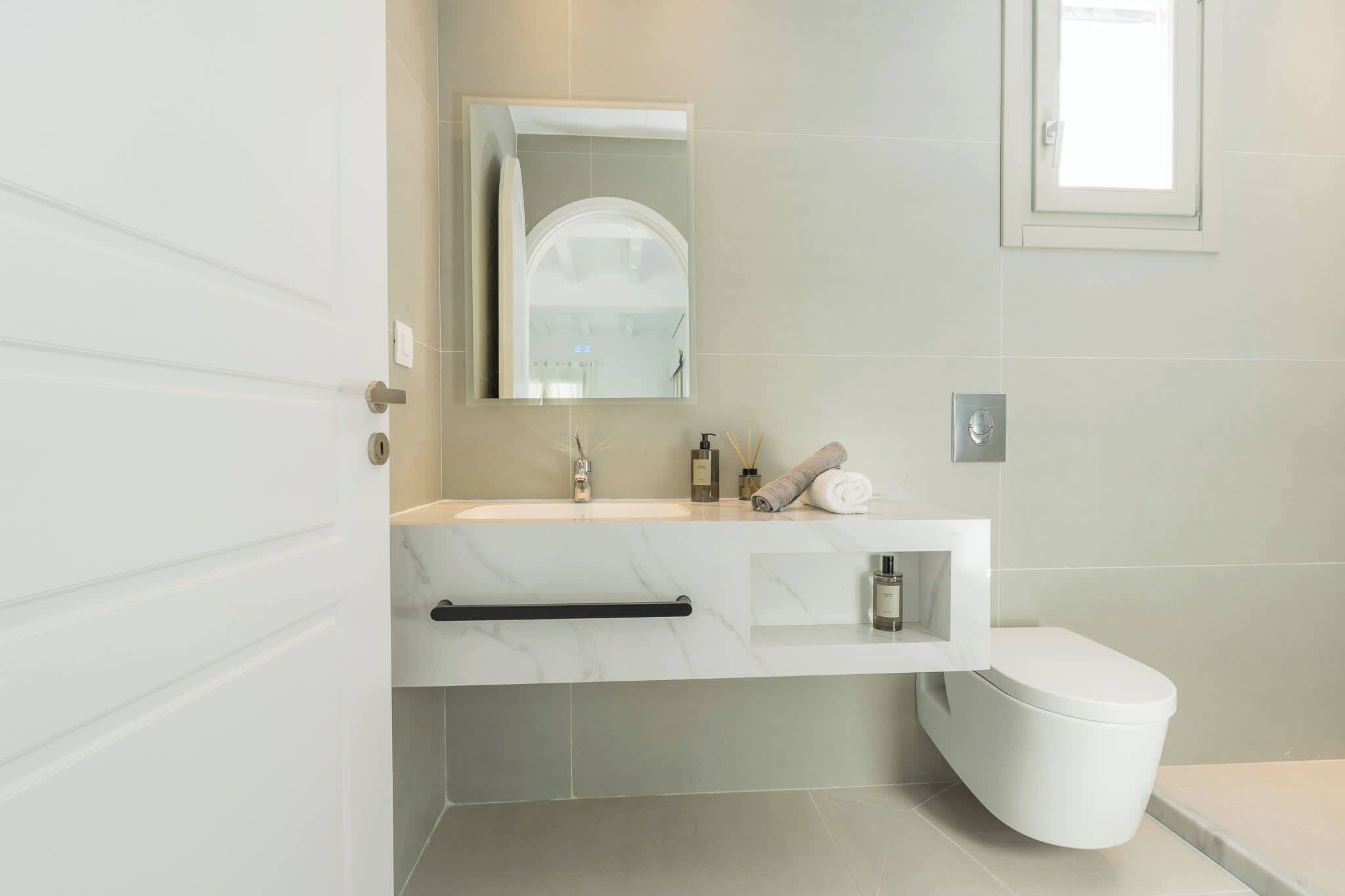 A modern bathroom with a white sink, mirror, and toilet.