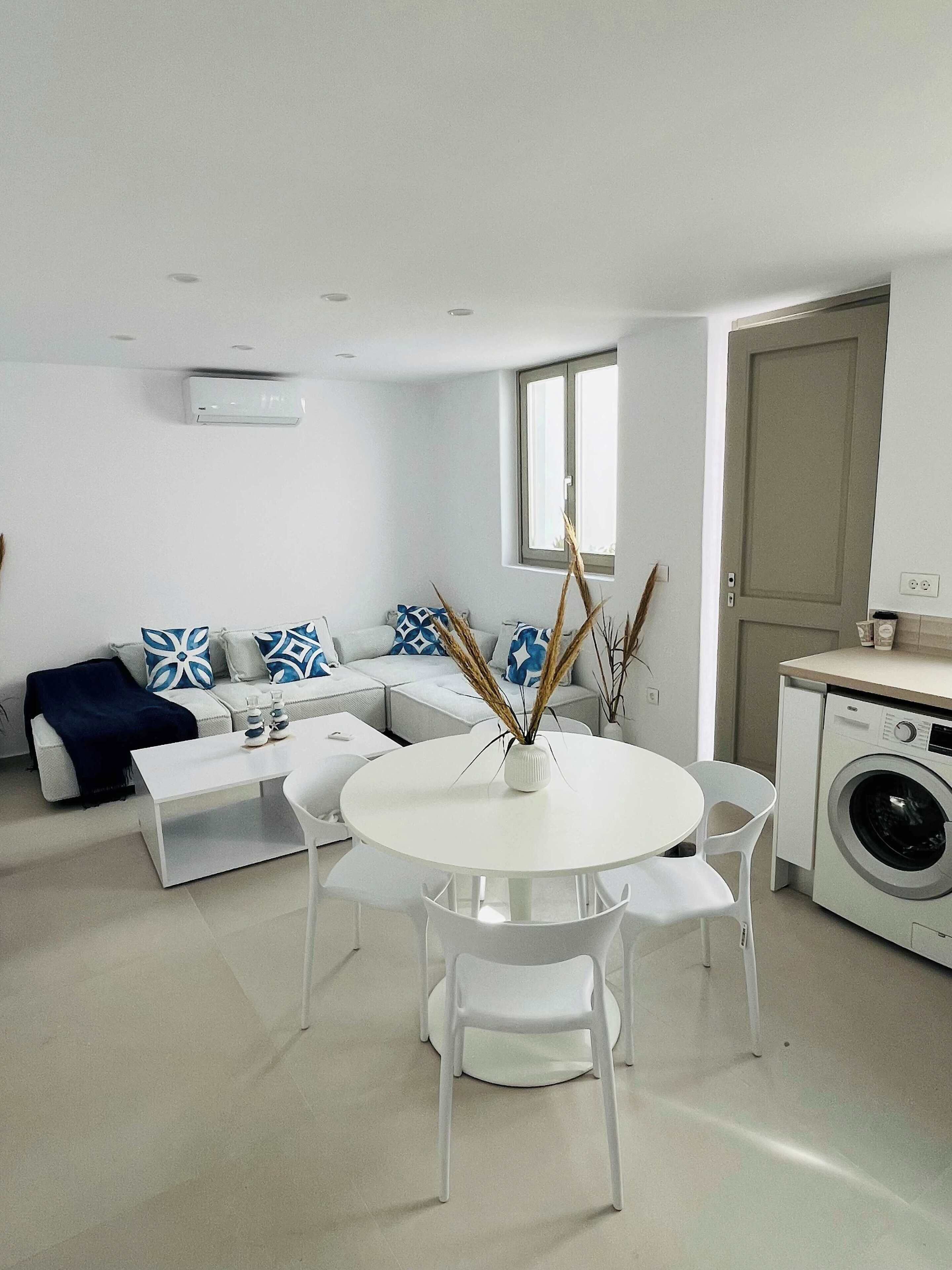 A modern living room with a sofa, a dining table with chairs, and a washing machine.