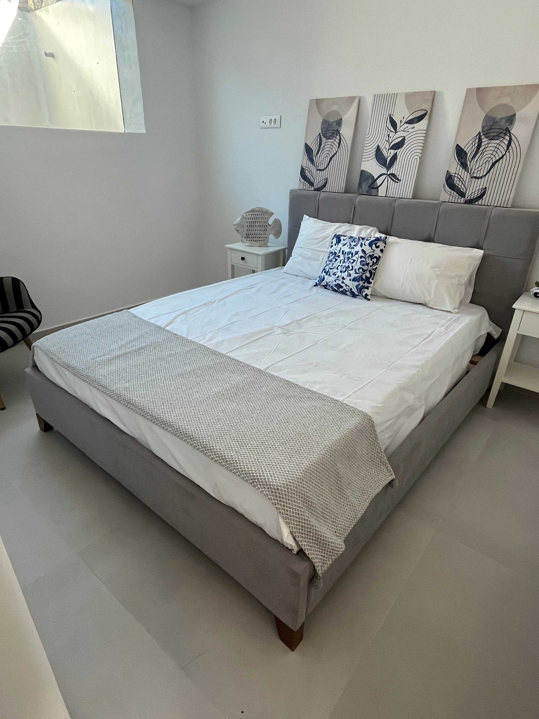 A modern bedroom with a large bed, a nightstand, a chair, and abstract wall art.